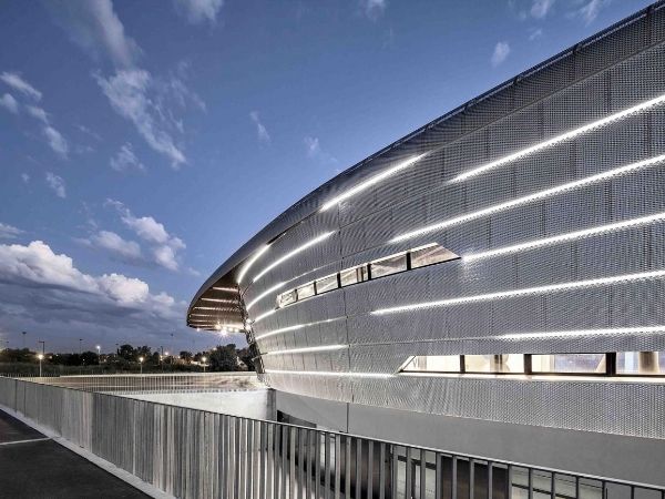 At night, stadium expanded metal facade is equipped with many strip lights.