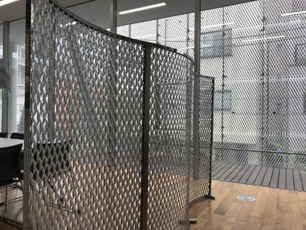 Expanded metal folding screen is placed behind the office desk.